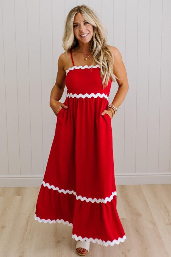 Woman wearing a red dress with white trim against a white wall.
