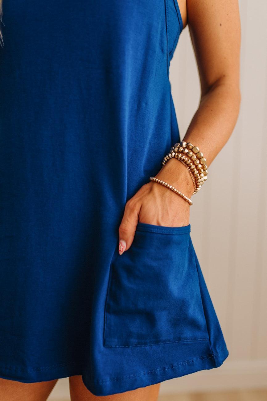 Person wearing a blue dress with a pocket, holding their hand in front of the dress.
