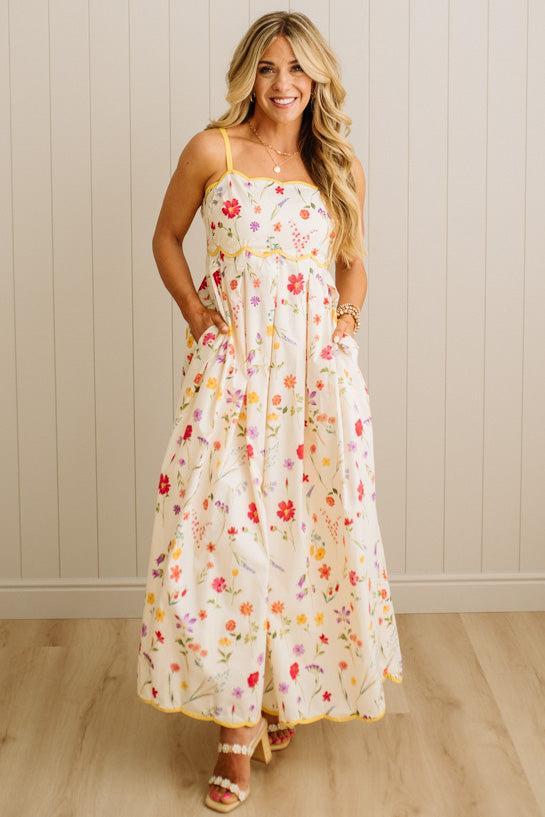 Woman wearing a floral dress standing against a light wooden paneled wall.