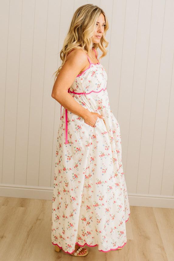 Woman wearing a floral dress with pink trim against a white paneled wall.