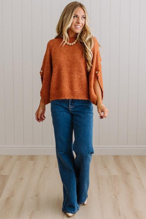 BLONDE WOMAN WEARING DARK JEANS IN A BRIGHTLY LIT STUDIO WITH A SOLID SWEATER FEATURING SCALLOP TRIM AND BUTTONS UP THE SLEEVE IN THE COLOR HEATHERED RUST.