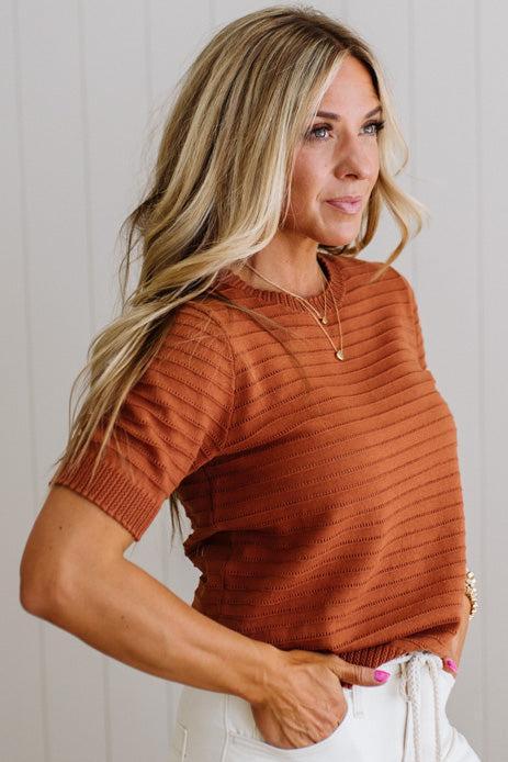 Woman wearing a rust-colored ribbed sweater against a light background