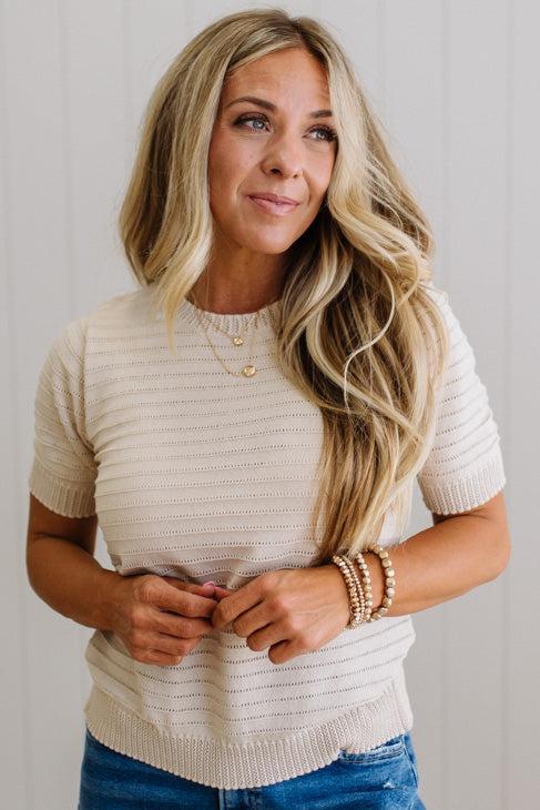Woman wearing a beige knit sweater and blue jeans against a plain background