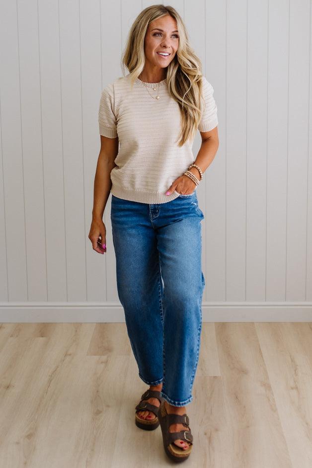 Woman wearing a beige knit sweater and blue jeans against a plain background