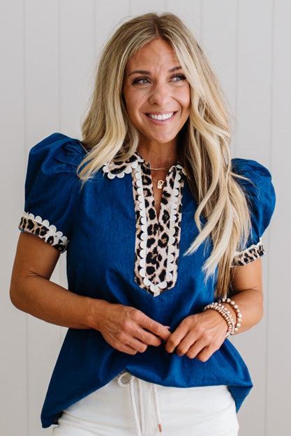 Woman wearing a blue blouse with leopard print details against a white background