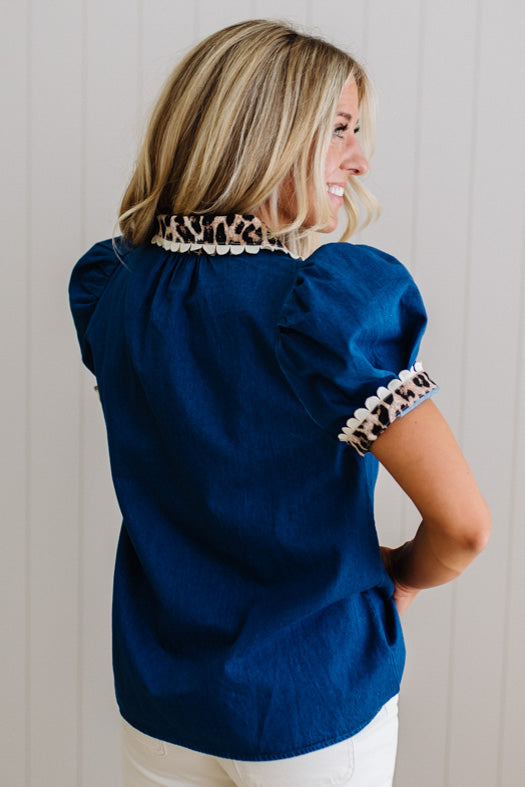 Woman wearing a blue blouse with leopard print trim against a plain background