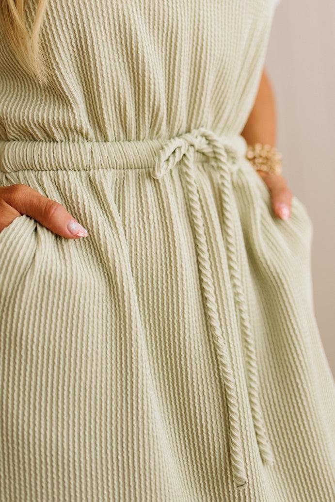 Close-up of a person wearing a light green ribbed dress with a belt.