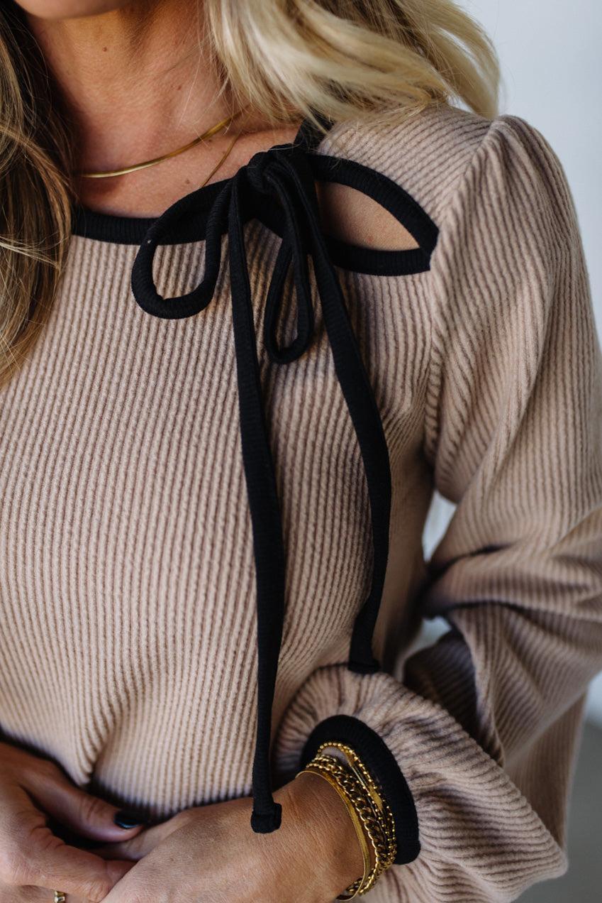 Beige ribbed sweater with black tie details worn by a person.