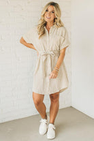 Blonde woman wearing a knee length striped shirt dress with button front and matching sash at waist.