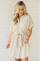 Blonde woman wearing a knee length striped shirt dress with button front and matching sash at waist.