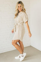 Blonde woman wearing a knee length striped shirt dress with button front and matching sash at waist.