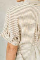 Blonde woman wearing a knee length striped shirt dress with button front and matching sash at waist.