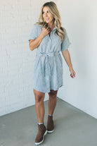 Blonde woman wearing a knee length striped shirt dress with button front and matching sash at waist.