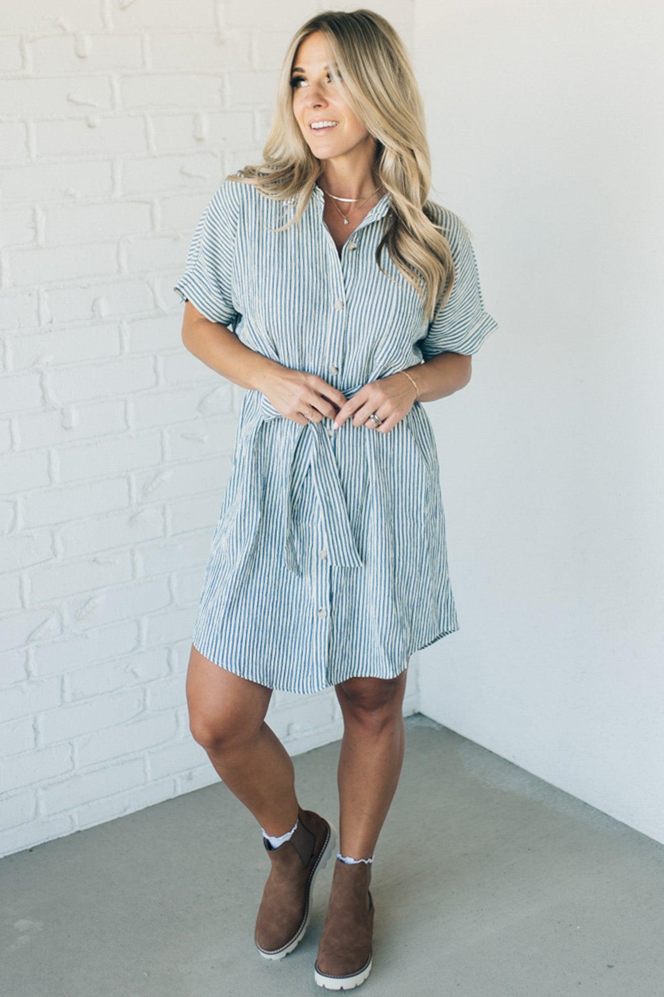 Blonde woman wearing a knee length striped shirt dress with button front and matching sash at waist.