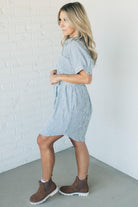 Blonde woman wearing a knee length striped shirt dress with button front and matching sash at waist.