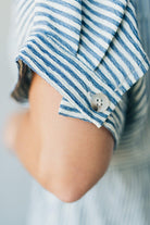 Blonde woman wearing a knee length striped shirt dress with button front and matching sash at waist.