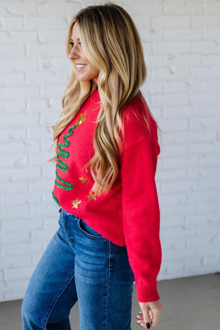 Woman wearing a red sweater with Christmas-themed designs against a white brick wall.