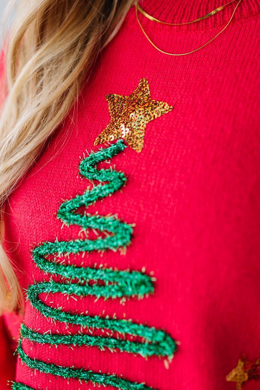Red sweater with green embroidered tree and gold star design.