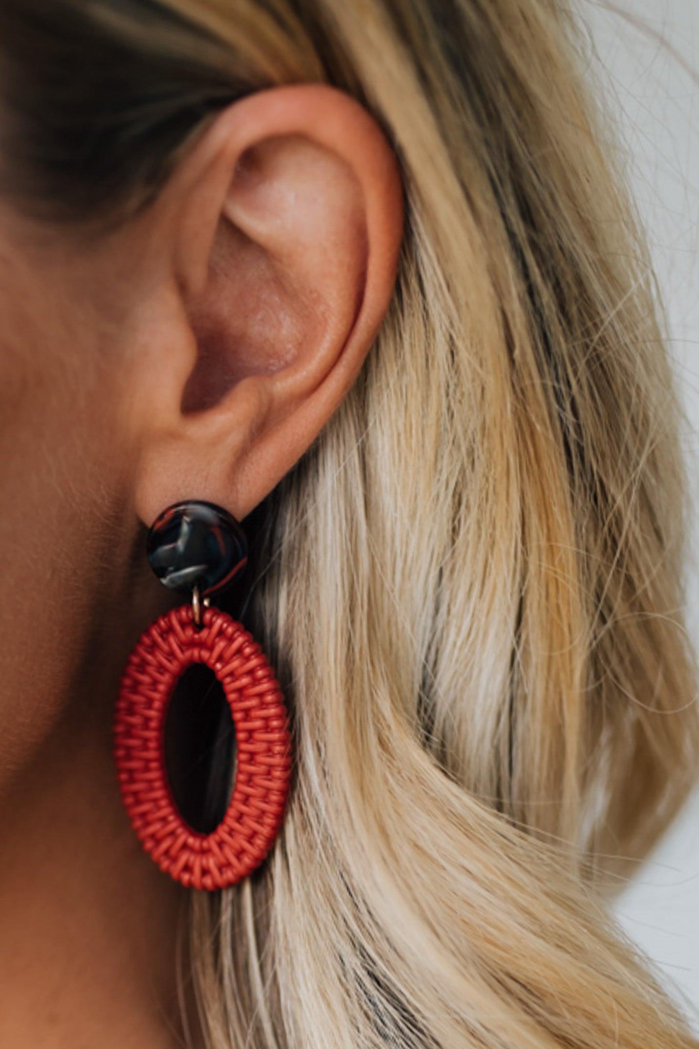 Close-up of a person wearing a red and black earring with blonde hair.