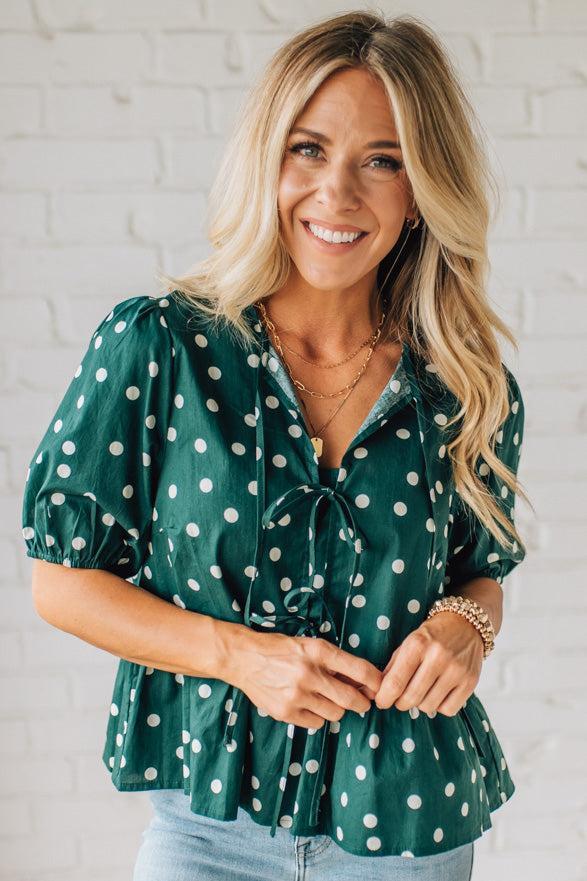 Woman wearing a green polka dot blouse against a white brick wall