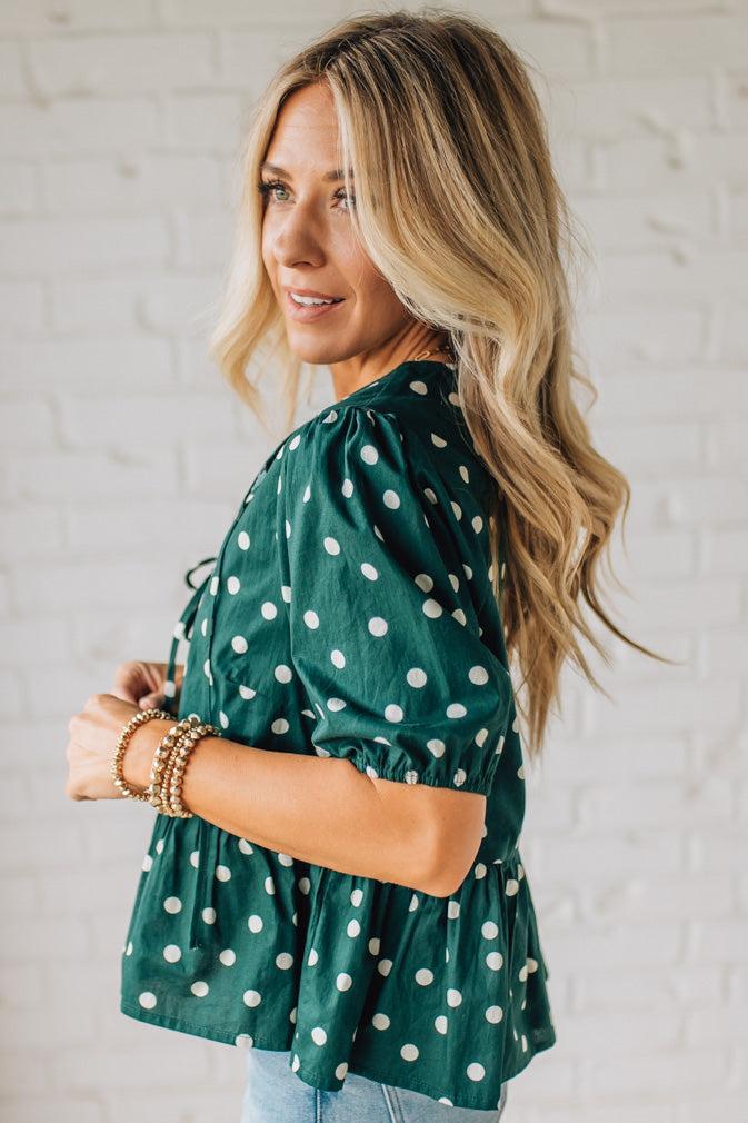 Woman wearing a green polka dot blouse against a white brick wall