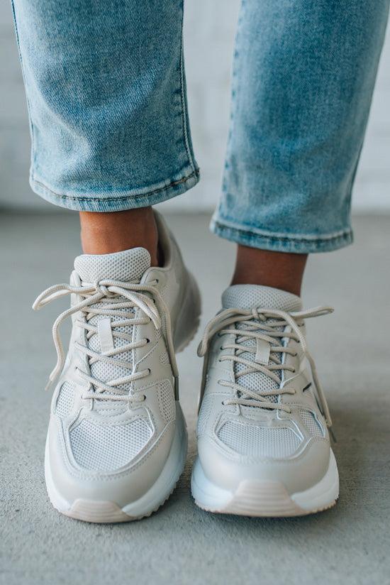 White sneakers worn with light blue jeans on a neutral background