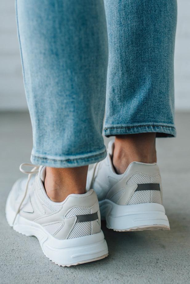 White sneakers with black accents worn with blue jeans on a neutral background