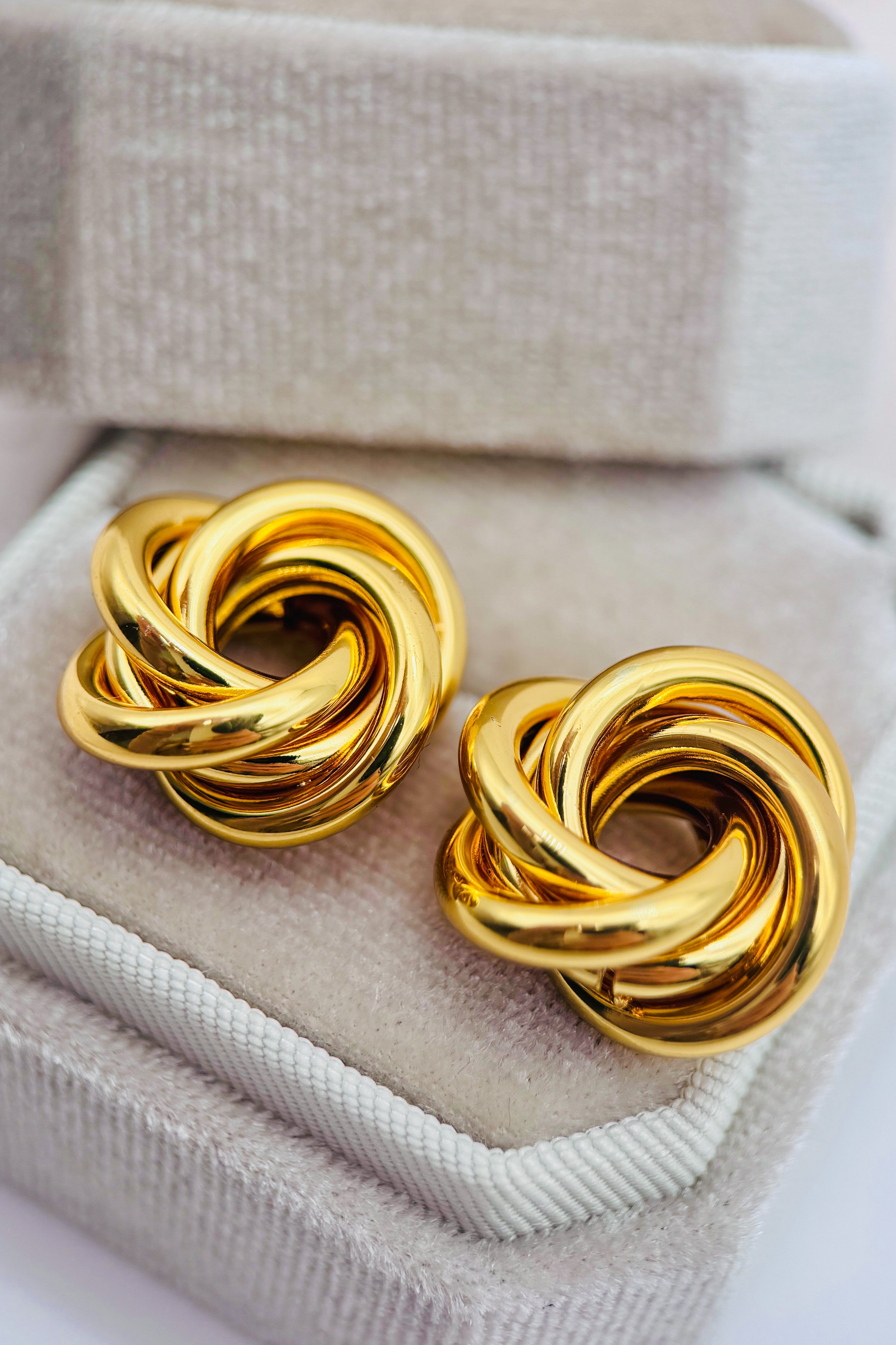 Pair of gold knot earrings on a textured surface