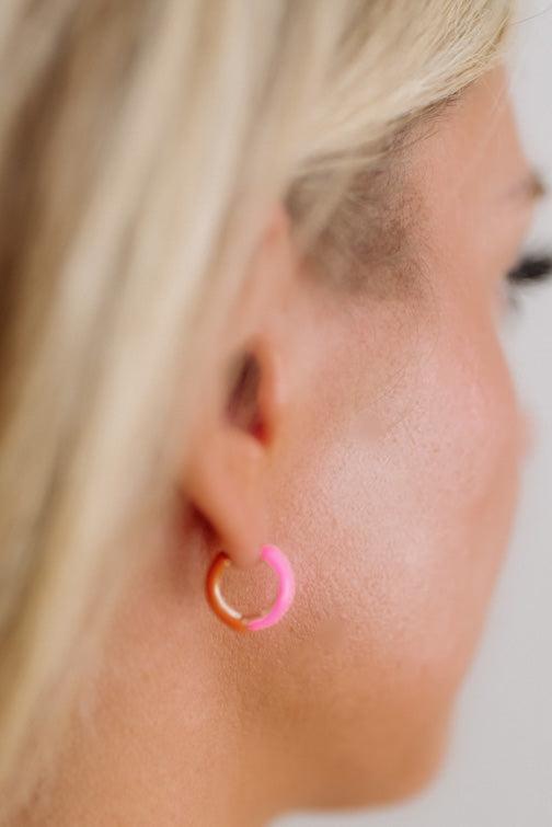 Close-up of a person wearing a gold and pink hoop earring.