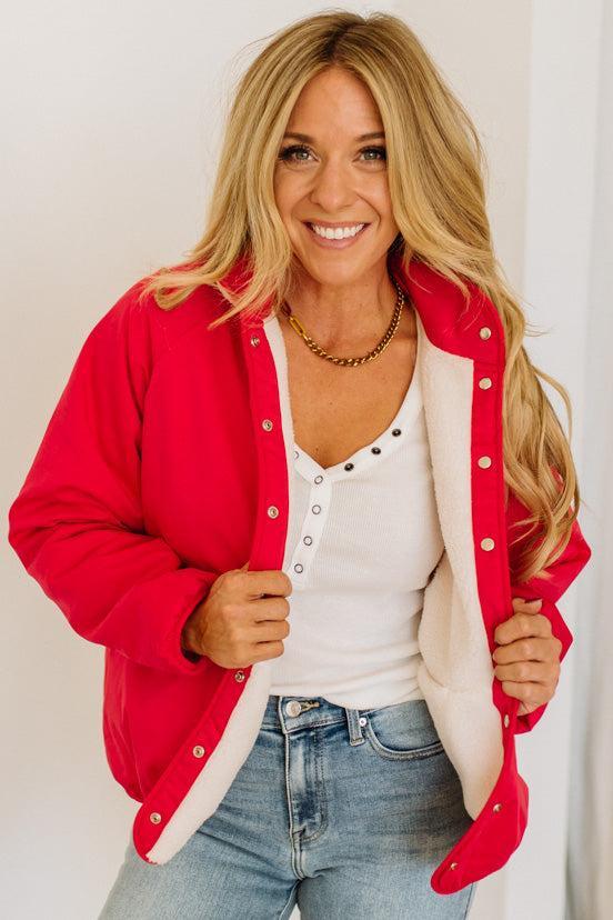 Woman wearing a red cardigan over a white shirt and blue jeans, smiling.
