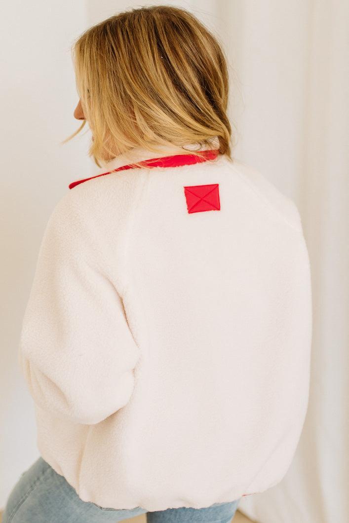 Person wearing a white jacket with a red patch on the back against a plain background