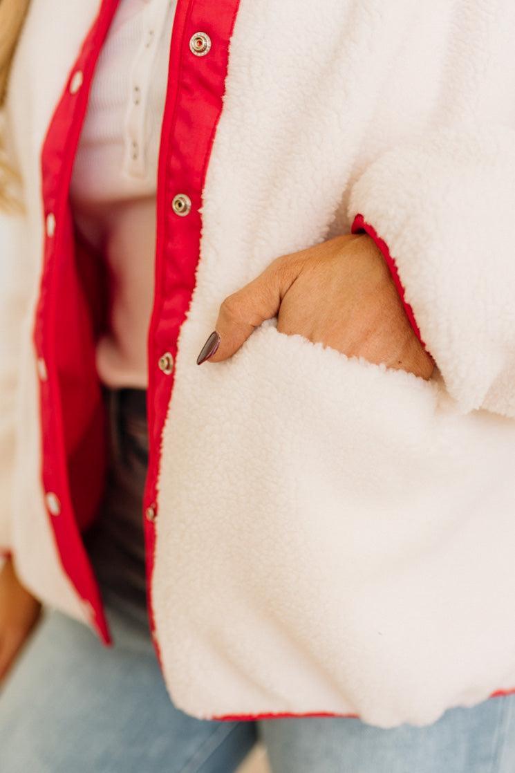 Close-up of a person wearing a white jacket with red trim and blue jeans.