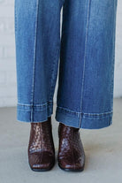 Cropped jeans worn with brown leather boots on a neutral background
