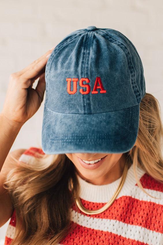 Blonde woman wearing a classic ball cap with USA embroidered at center front.