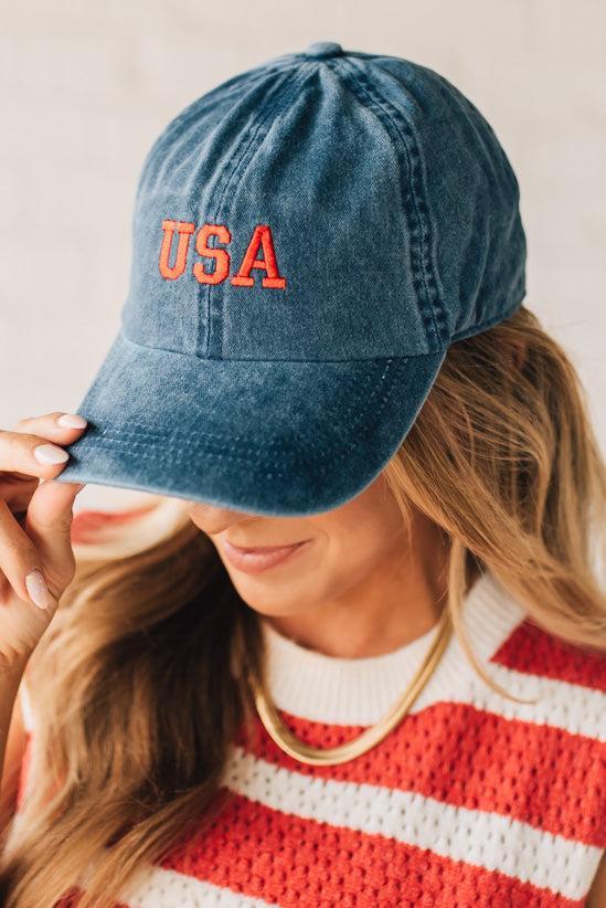 Blonde woman wearing a classic ball cap with USA embroidered at center front.