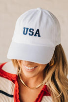 Blonde woman wearing a classic ball cap with USA embroidered at center front.