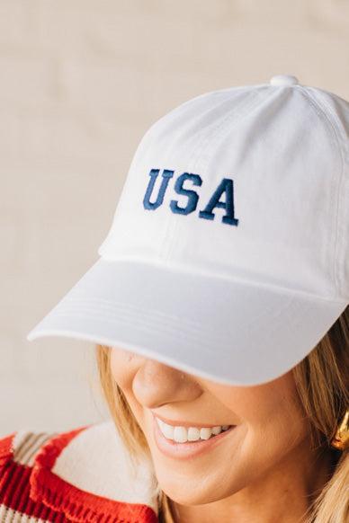 Blonde woman wearing a classic ball cap with USA embroidered at center front.