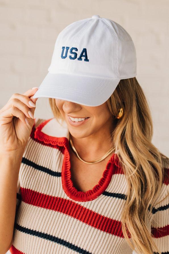 Blonde woman wearing a classic ball cap with USA embroidered at center front.