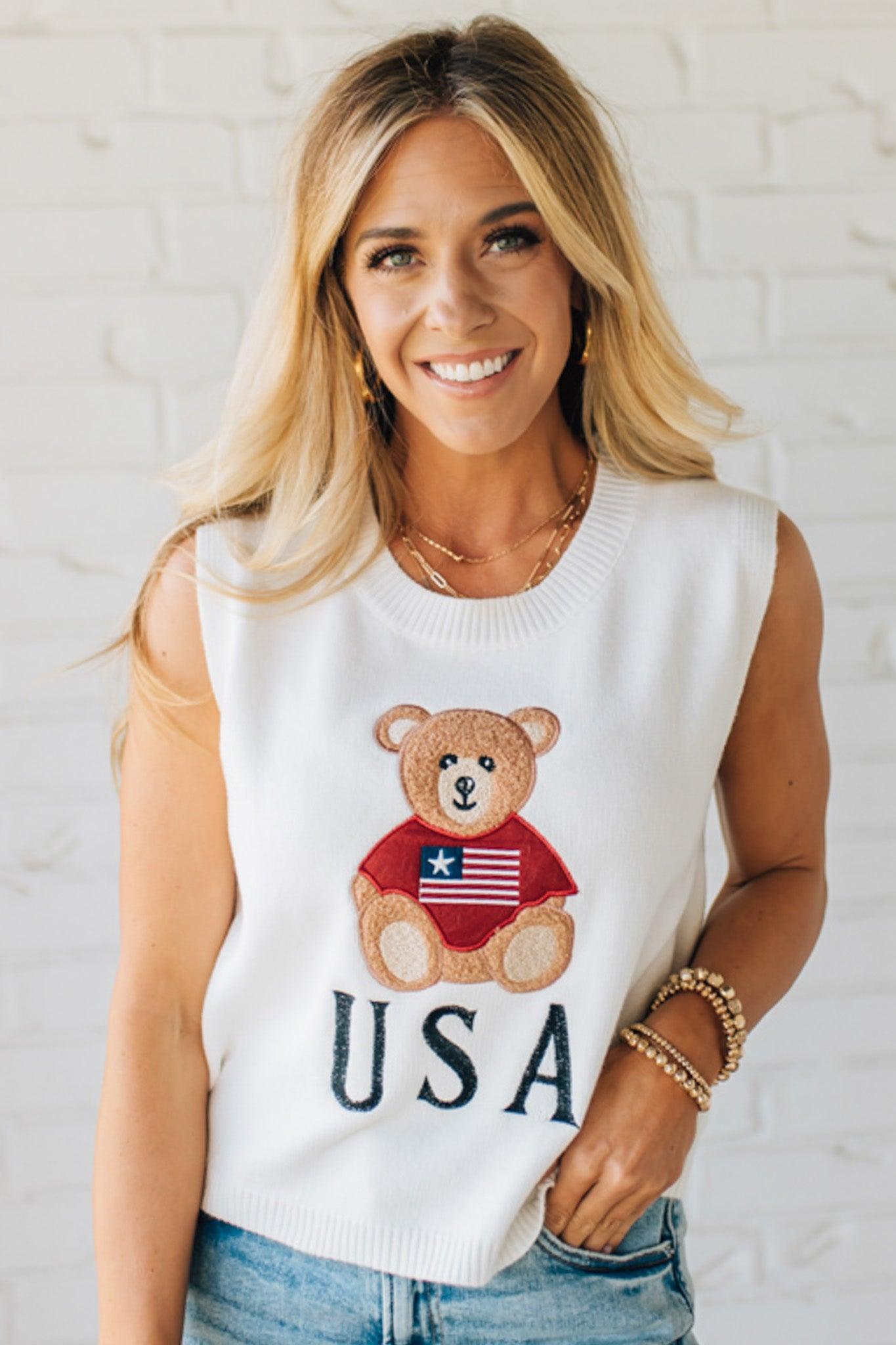 BLONDE WOMAN IN DENIM SHORTS WEARING A TEDDY BEAR WEARING AN AMERICAN FLAG WITH USA EMBROIDERY LETTERING FOURTH OF JULY SWEATER TANK TOP.