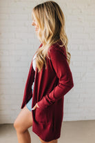 Woman wearing a burgundy cardigan in front of a white brick wall