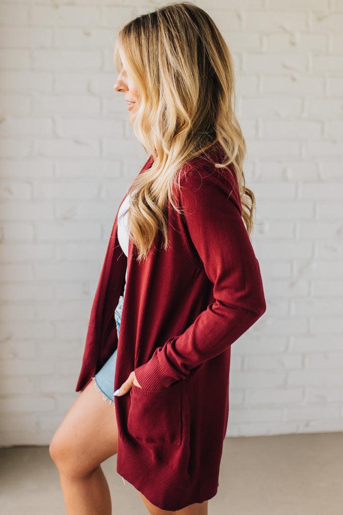 Woman wearing a burgundy cardigan in front of a white brick wall