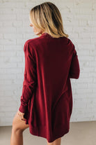 Woman wearing a burgundy oversized shirt against a white brick wall.