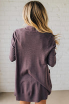 Person wearing a purple cardigan against a white brick wall