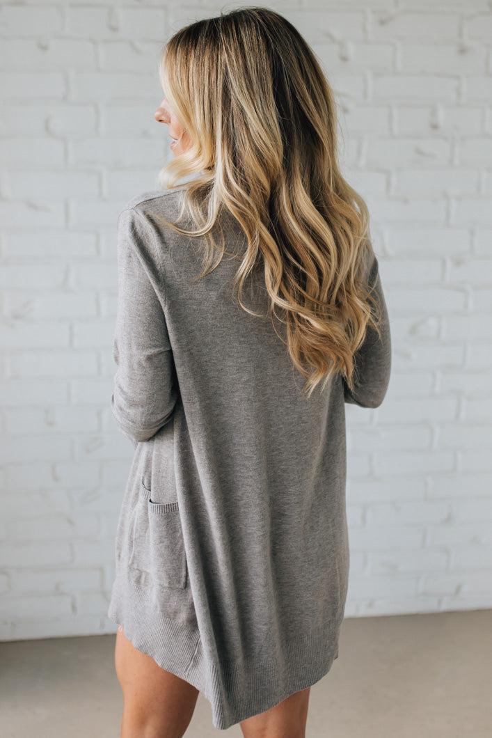 Woman wearing a gray cardigan against a white brick wall