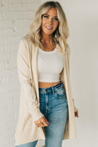 A woman wearing a long black cardigan with pockets, paired with a white top and blue jeans, standing in a field.