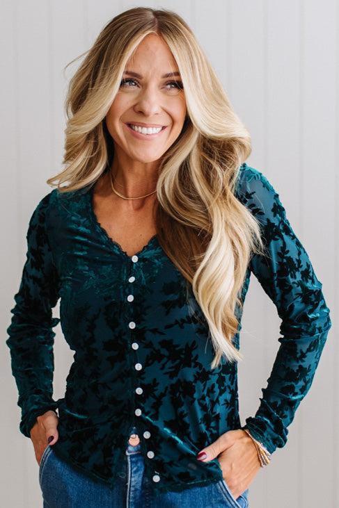 BLONDE WOMAN IN DARK JEANS WEARING A ROMANTIC VELVET BURNOUT TOP WITH FEATURES LIKE, BURNOUT VELVET MESH FABRICATION, SCALLOPED LACE EDGE ACCENTS, FUNCTIONAL BUTTONS AND LONG SLEEVES