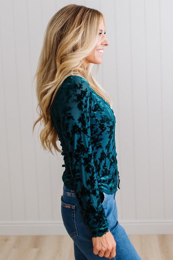 BLONDE WOMAN IN DARK JEANS WEARING A ROMANTIC VELVET BURNOUT TOP WITH FEATURES LIKE, BURNOUT VELVET MESH FABRICATION, SCALLOPED LACE EDGE ACCENTS, FUNCTIONAL BUTTONS AND LONG SLEEVES
