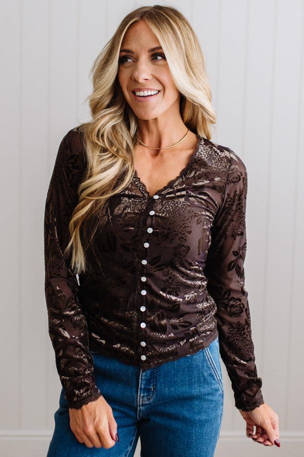 BLONDE WOMAN IN DARK JEANS WEARING A ROMANTIC VELVET BURNOUT TOP WITH FEATURES LIKE, BURNOUT VELVET MESH FABRICATION, SCALLOPED LACE EDGE ACCENTS, FUNCTIONAL BUTTONS AND LONG SLEEVES
