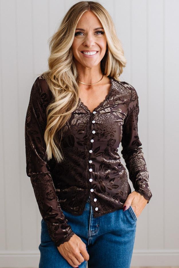 BLONDE WOMAN IN DARK JEANS WEARING A ROMANTIC VELVET BURNOUT TOP WITH FEATURES LIKE, BURNOUT VELVET MESH FABRICATION, SCALLOPED LACE EDGE ACCENTS, FUNCTIONAL BUTTONS AND LONG SLEEVES