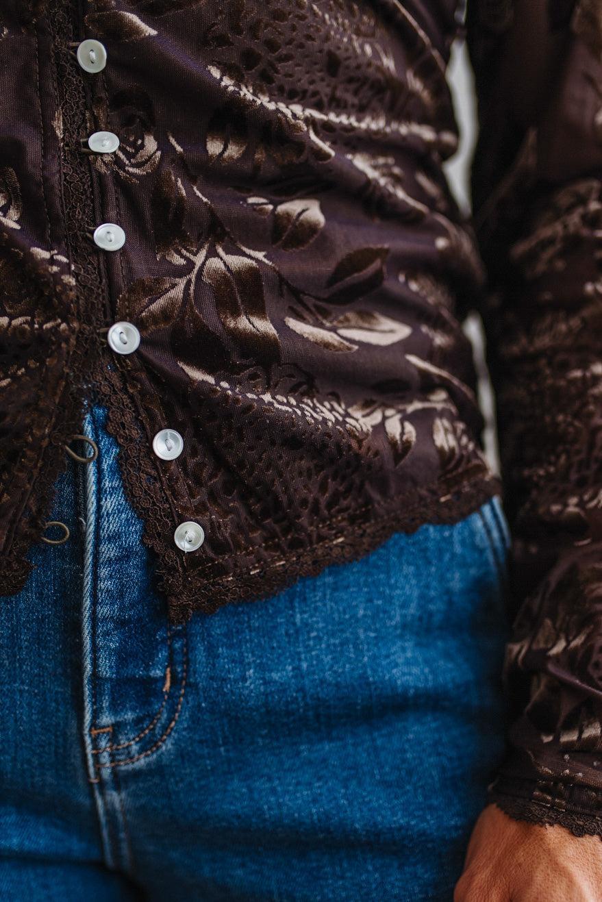BLONDE WOMAN IN DARK JEANS WEARING A ROMANTIC VELVET BURNOUT TOP WITH FEATURES LIKE, BURNOUT VELVET MESH FABRICATION, SCALLOPED LACE EDGE ACCENTS, FUNCTIONAL BUTTONS AND LONG SLEEVES